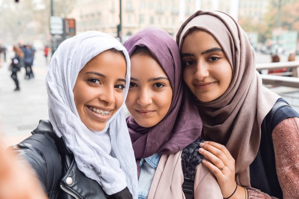 Three middle school aged girls wearing hijab smile at the camera.